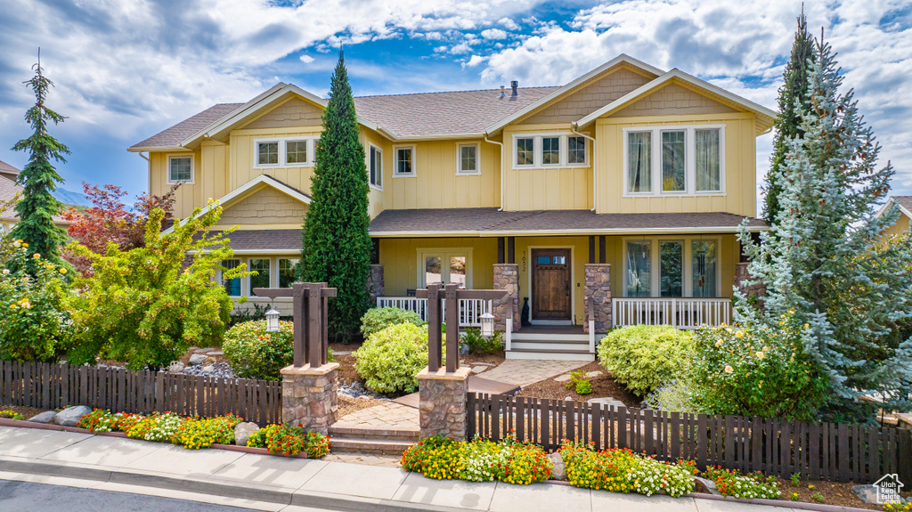 Craftsman-style house with covered porch, stone siding, and a fenced front yard