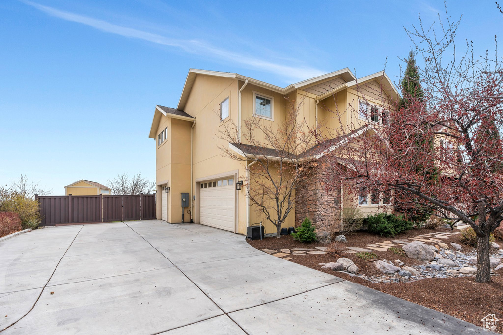 View of side of property featuring driveway, stucco siding, fence, and an attached garage