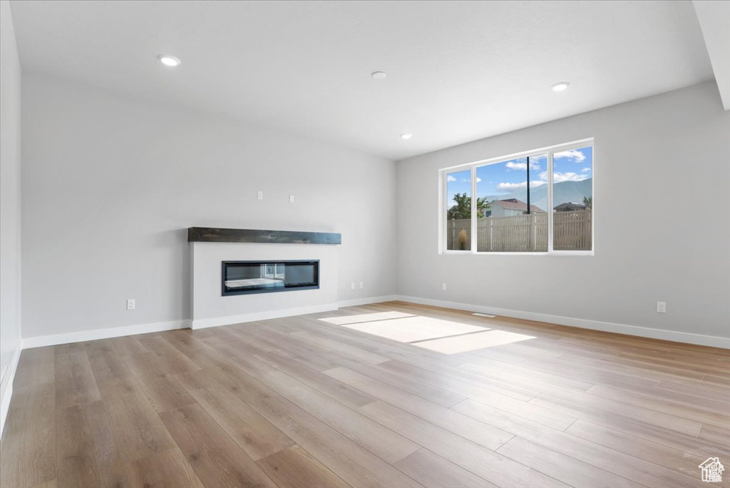 Unfurnished living room with a glass covered fireplace, baseboards, and wood finished floors