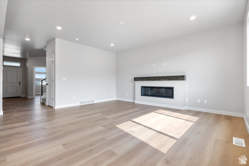 Unfurnished living room with visible vents, a glass covered fireplace, and light wood-type flooring