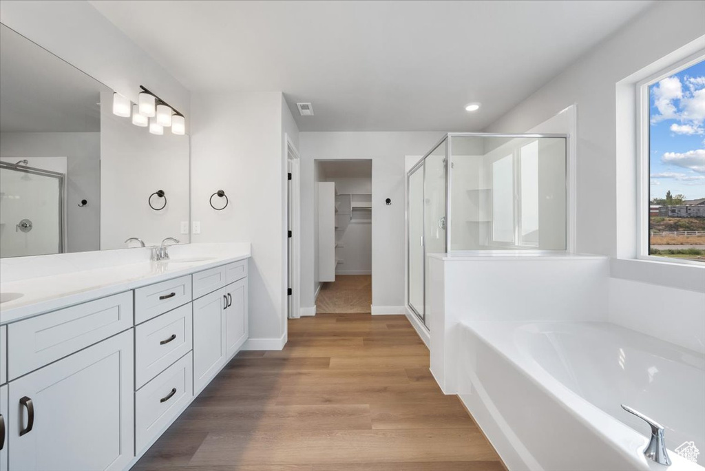 Full bathroom featuring double vanity, a sink, a stall shower, and wood finished floors