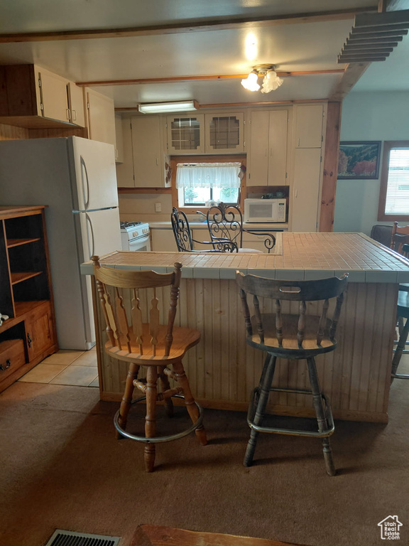 Kitchen featuring a breakfast bar area, visible vents, light colored carpet, tile counters, and white appliances