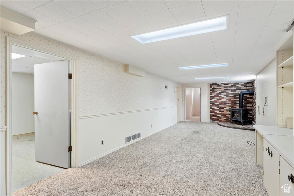 Interior space with wallpapered walls, a wood stove, wainscoting, light colored carpet, and visible vents
