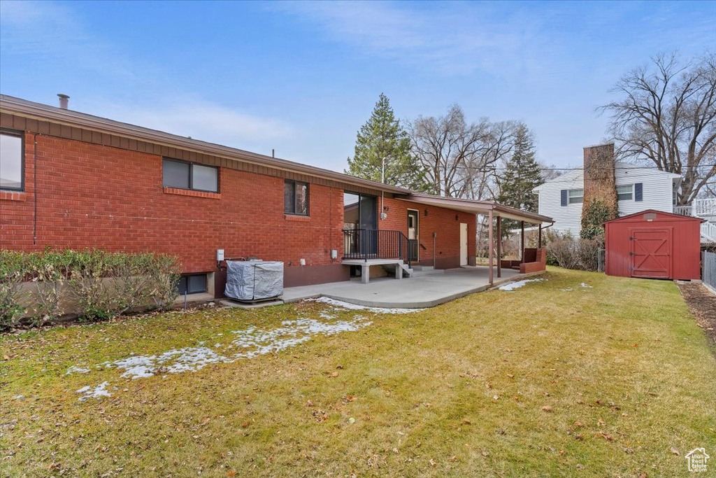 Back of property with a storage shed, a patio, brick siding, an outbuilding, and a yard