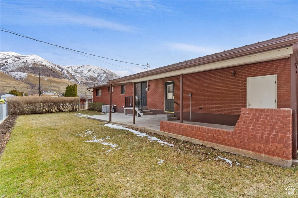 Rear view of house with entry steps, a patio, brick siding, a lawn, and a mountain view