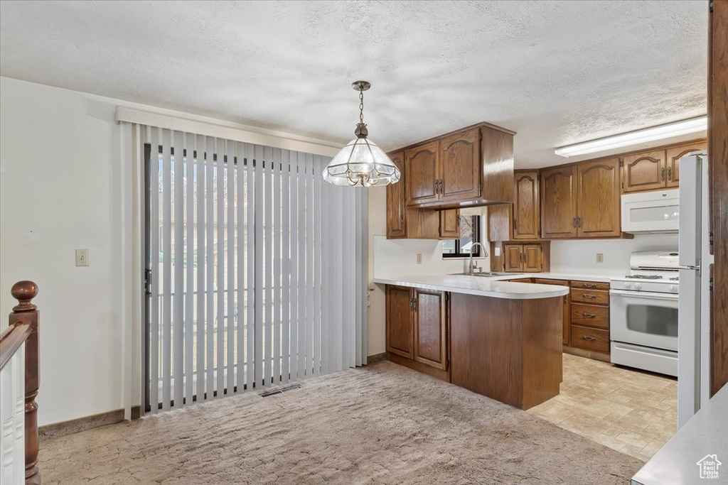 Kitchen with a sink, a peninsula, brown cabinets, white appliances, and visible vents