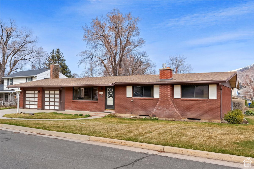 Ranch-style house with an attached garage, a chimney, brick siding, a front lawn, and driveway