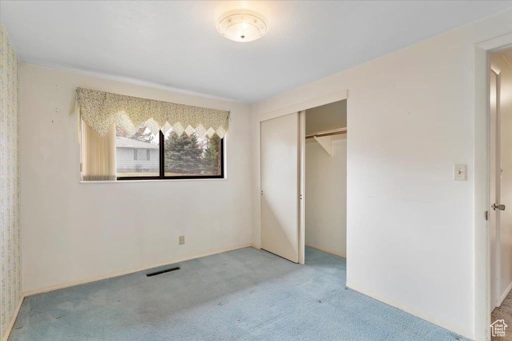 Unfurnished bedroom featuring light carpet, baseboards, visible vents, and a closet
