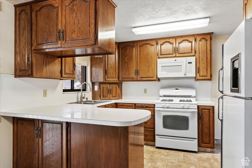 Kitchen featuring light countertops, a sink, a peninsula, brown cabinetry, and white appliances