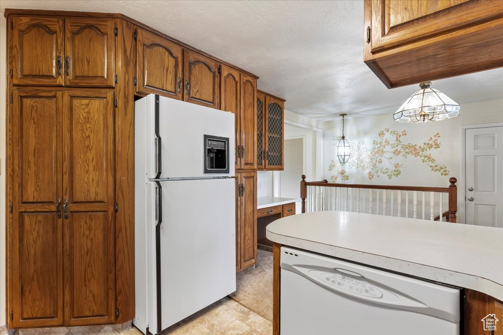 Kitchen featuring light countertops, brown cabinets, pendant lighting, and white appliances