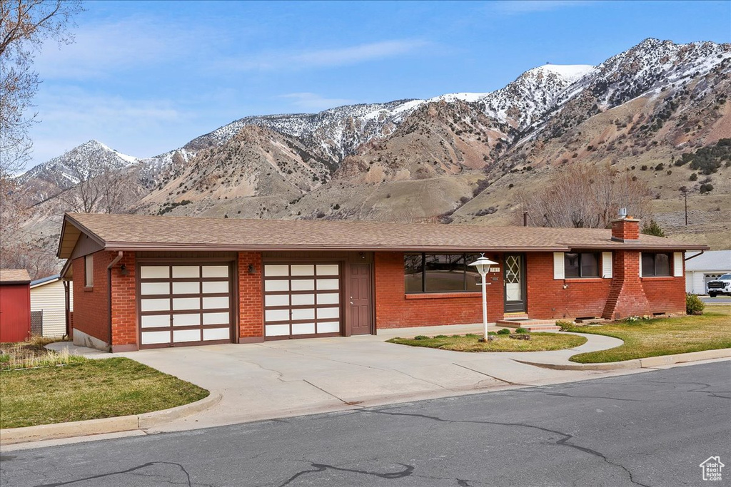Ranch-style house featuring driveway, a mountain view, brick siding, a garage, and a chimney