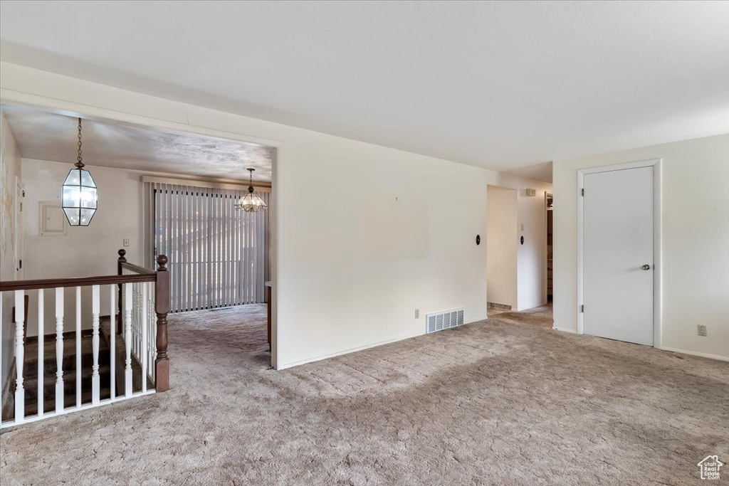Carpeted empty room with an inviting chandelier and visible vents