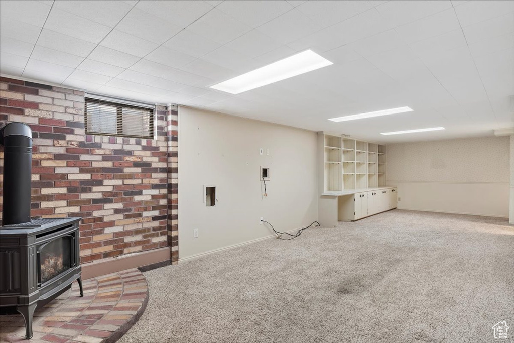 Finished basement featuring baseboards, a wood stove, carpet, and brick wall