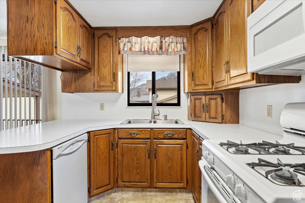 Kitchen featuring light countertops, a sink, brown cabinetry, and white appliances