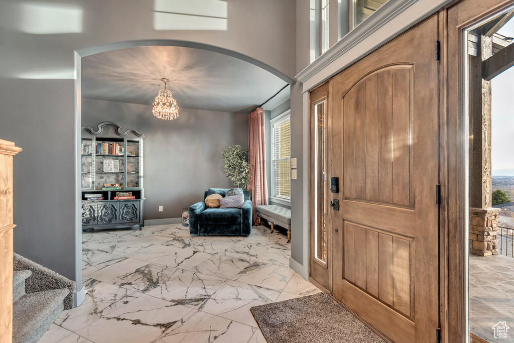 Entryway with a chandelier, baseboards, marble finish floor, stairs, and arched walkways