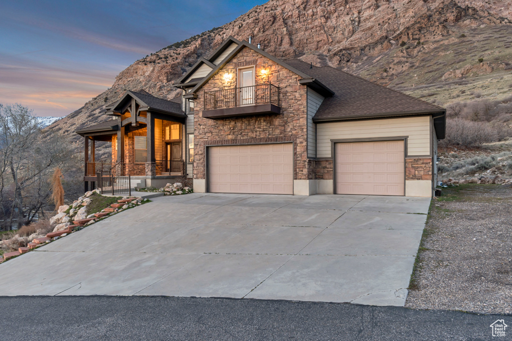 Chalet / cabin featuring an attached garage, stone siding, a balcony, driveway, and a porch