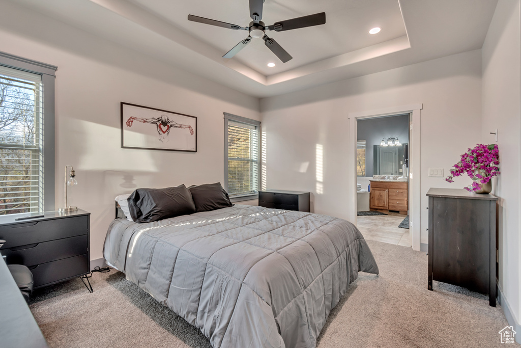 Bedroom with a tray ceiling, light carpet, ensuite bath, baseboards, and recessed lighting