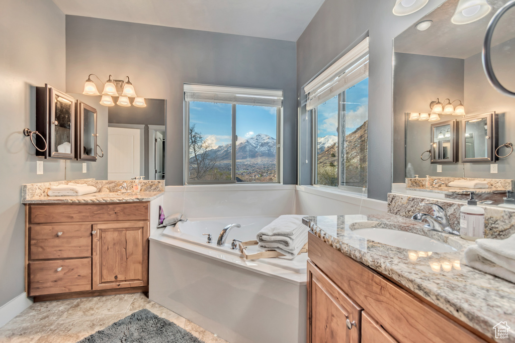 Bathroom with a sink, a notable chandelier, two vanities, and a garden tub