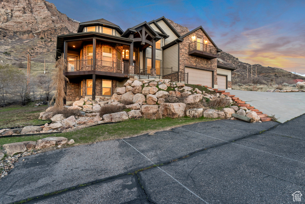 View of front of home with stone siding, driveway, an attached garage, and a balcony