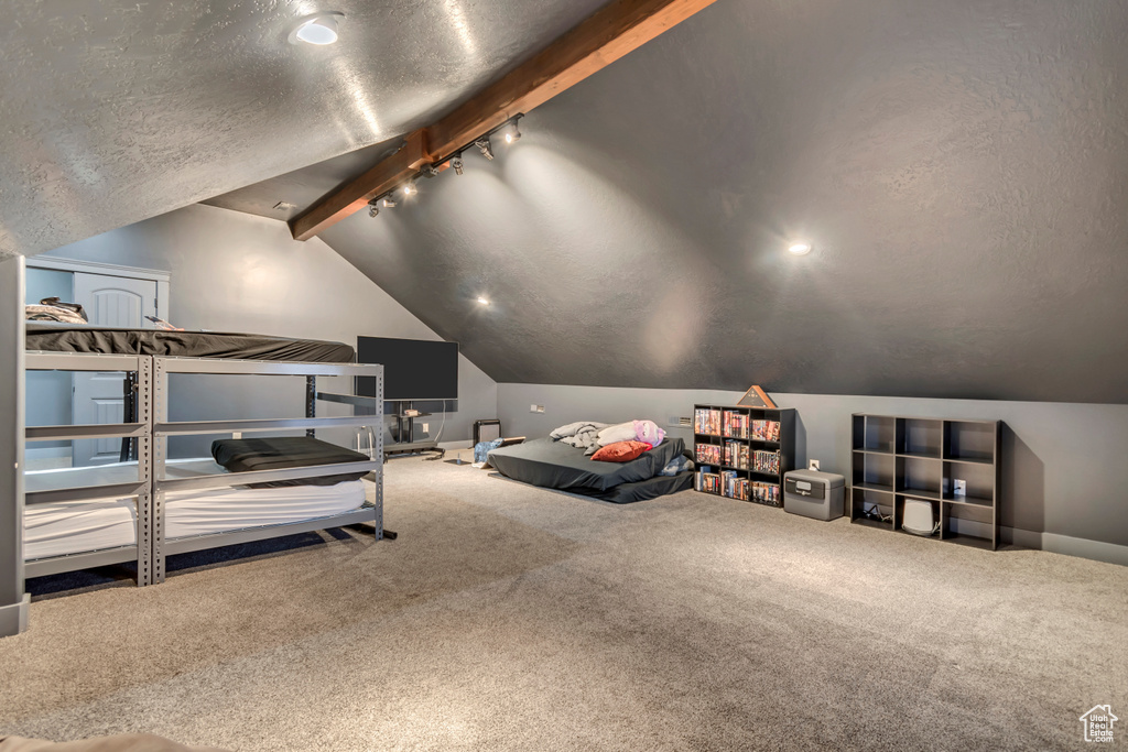 Bedroom featuring vaulted ceiling with beams, track lighting, carpet flooring, and a textured ceiling