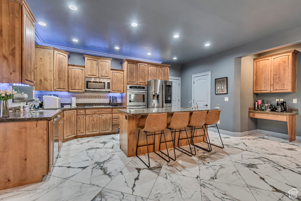 Kitchen with decorative backsplash, a kitchen island with sink, a kitchen bar, recessed lighting, and appliances with stainless steel finishes