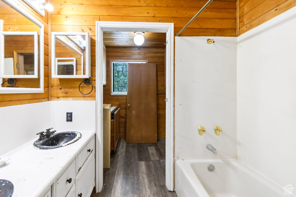 Bathroom with wood finished floors, double vanity,  shower combination, and wooden walls