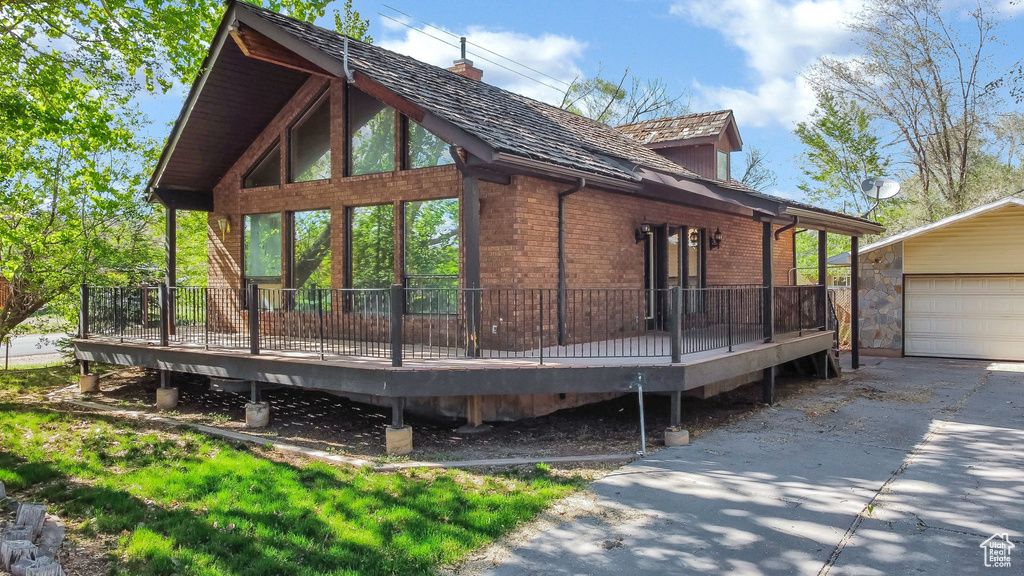 View of side of home with a deck, brick siding, an outbuilding, and a chimney