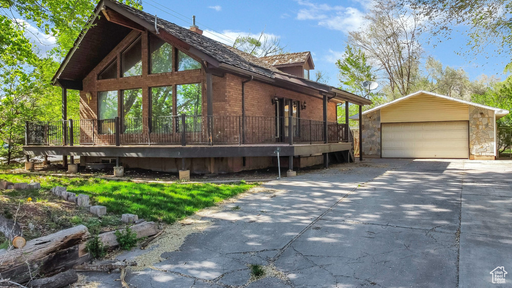 View of home\'s exterior featuring a detached garage, an outdoor structure, brick siding, and a wooden deck