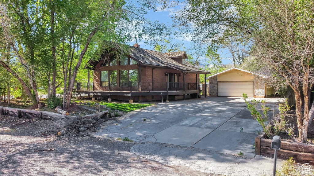 View of side of property featuring an outdoor structure, a detached garage, driveway, and a wooden deck