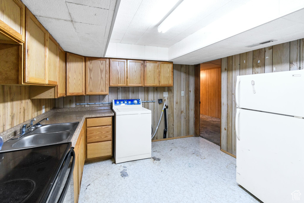Kitchen with freestanding refrigerator, washer / dryer, a sink, wooden walls, and light flooring