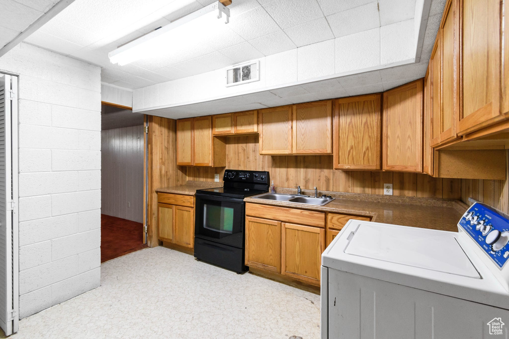 Kitchen featuring washer / clothes dryer, black range with electric cooktop, a sink, and wood walls
