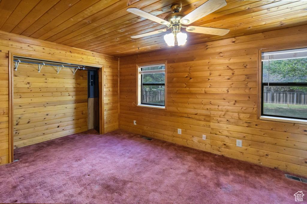 Empty room with wooden ceiling, wooden walls, carpet flooring, and a ceiling fan