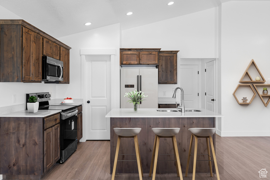 Kitchen featuring appliances with stainless steel finishes, light wood-style flooring, dark brown cabinetry, lofted ceiling, and recessed lighting