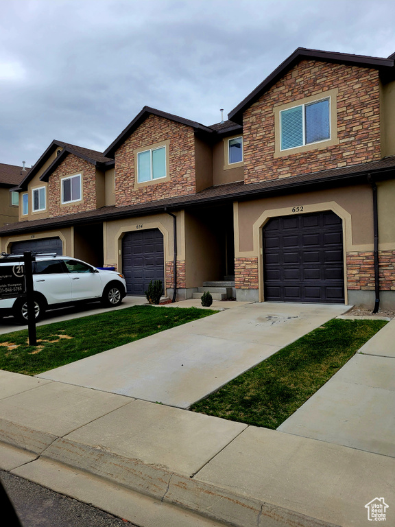 View of property featuring an attached garage, stucco siding, stone siding, and concrete driveway