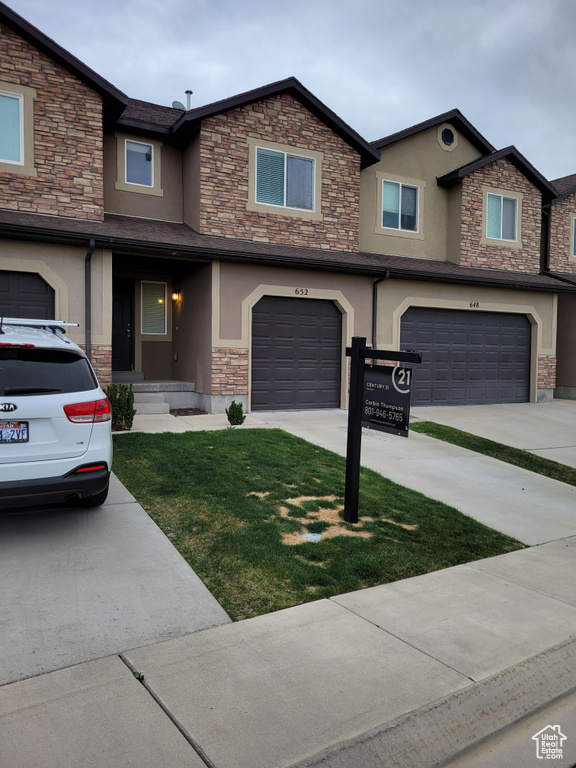 View of property with stucco siding, a garage, stone siding, and concrete driveway