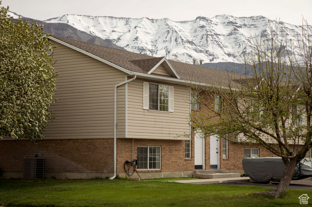 Exterior space with central air condition unit, a mountain view, brick siding, and a lawn