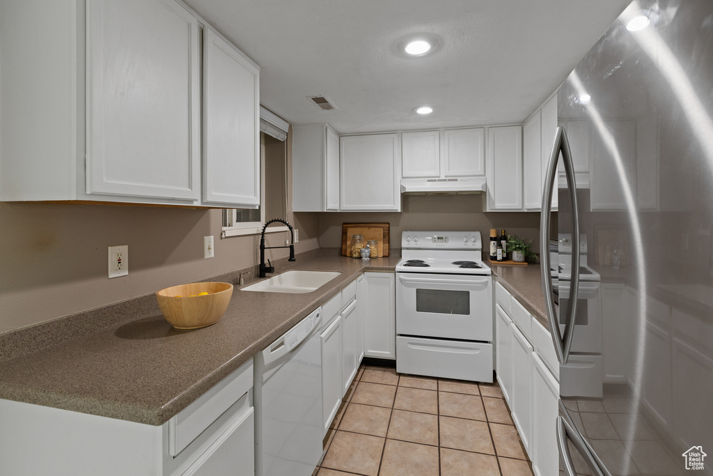 Kitchen featuring white appliances, visible vents, white cabinets, under cabinet range hood, and a sink