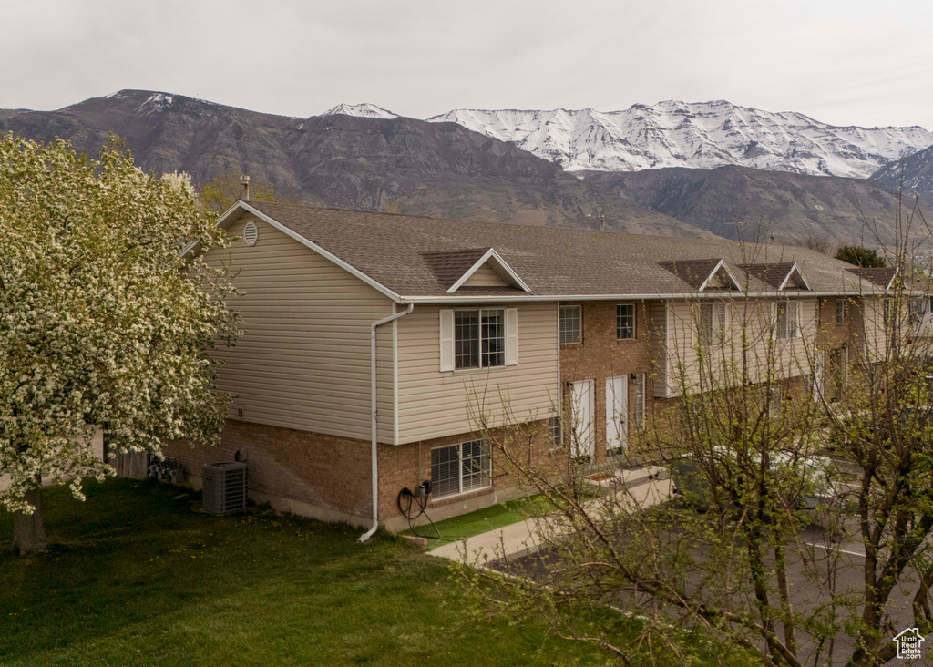 Exterior space with brick siding, a mountain view, a lawn, and central air condition unit