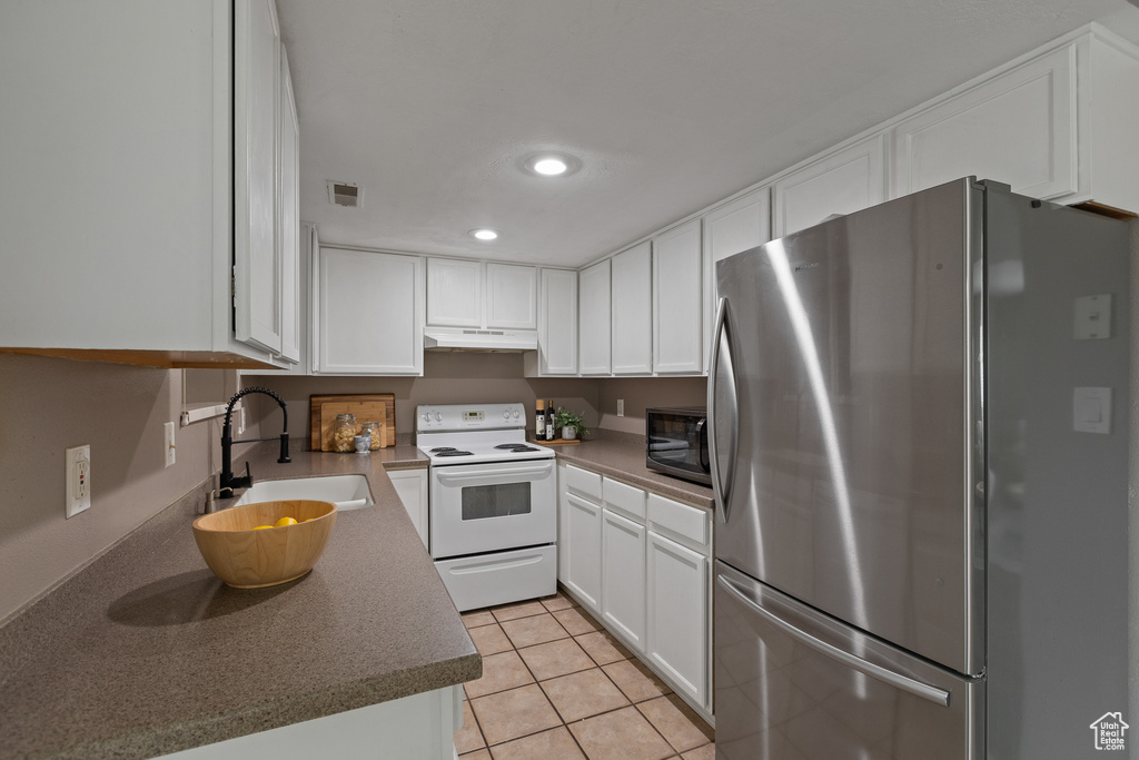 Kitchen featuring white electric range, freestanding refrigerator, black microwave, visible vents, and a sink