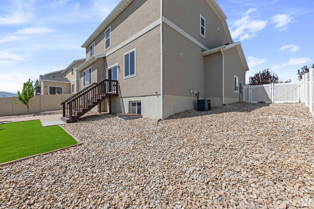 Back of house with central air condition unit, a gate, a fenced backyard, and stucco siding