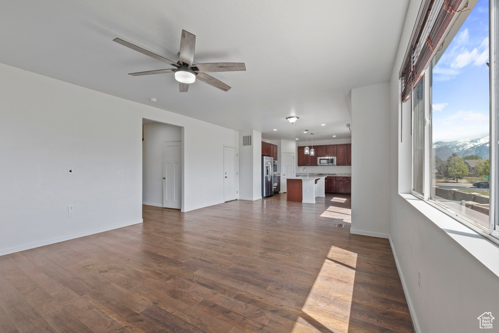 Unfurnished living room with a ceiling fan, baseboards, and dark wood finished floors