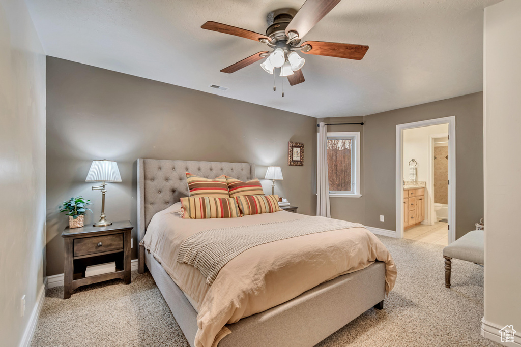 Bedroom featuring baseboards, ensuite bath, visible vents, a ceiling fan, and light carpet