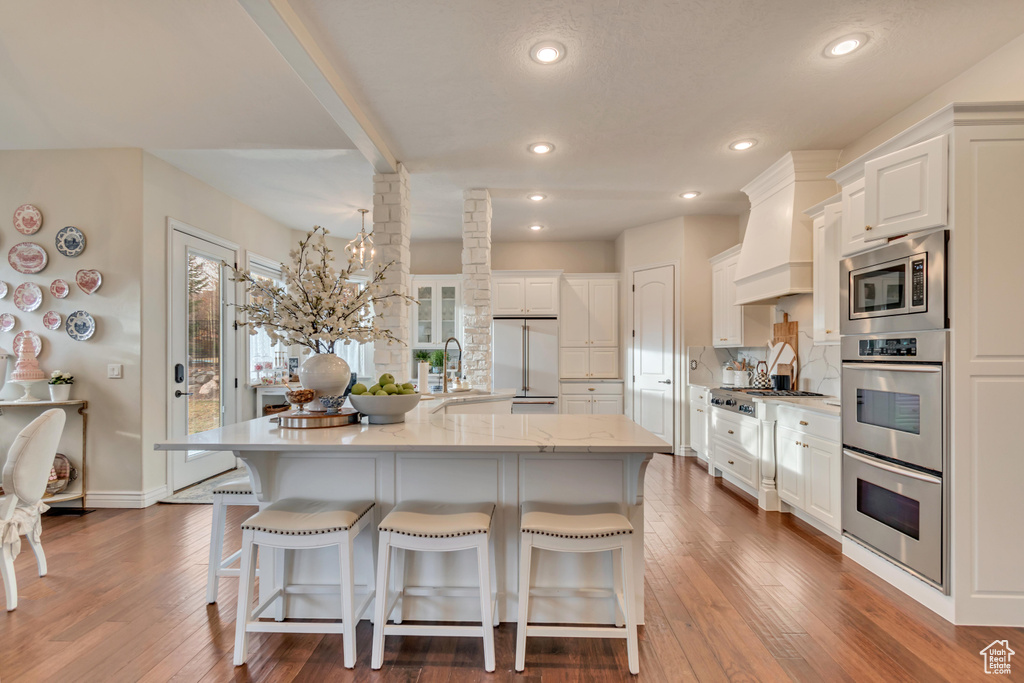 Kitchen with premium range hood, dark wood-style flooring, a kitchen breakfast bar, and built in appliances