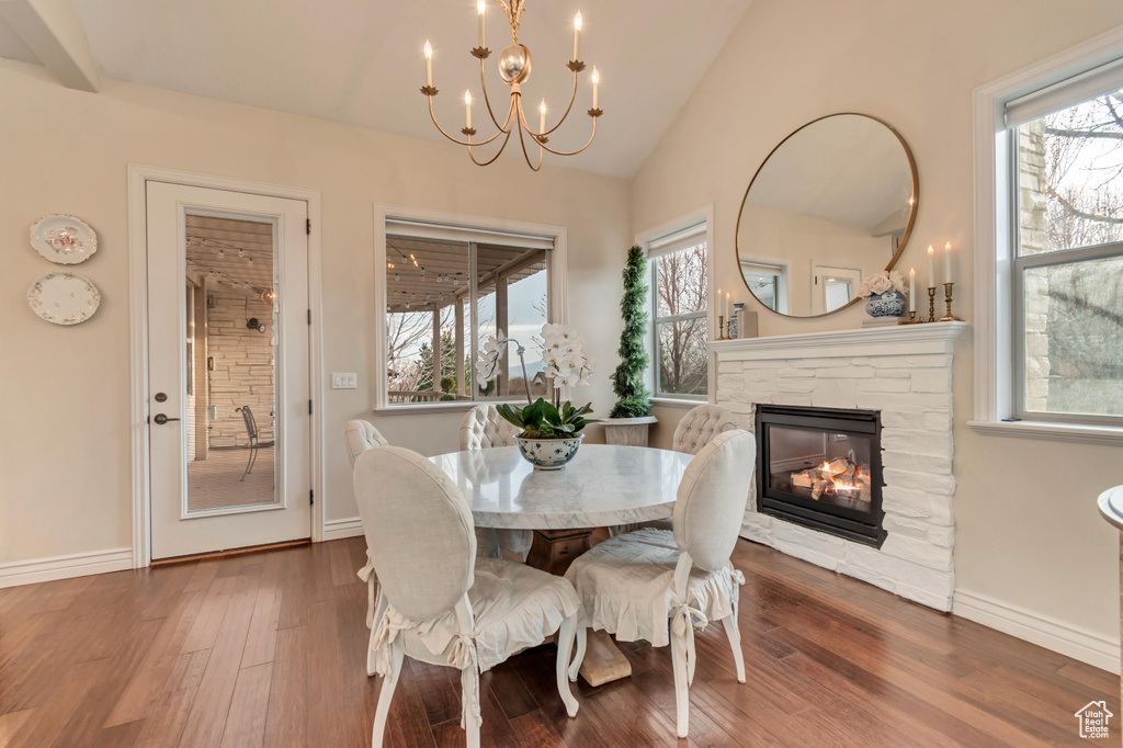 Dining area featuring a notable chandelier, a fireplace, wood finished floors, lofted ceiling, and baseboards
