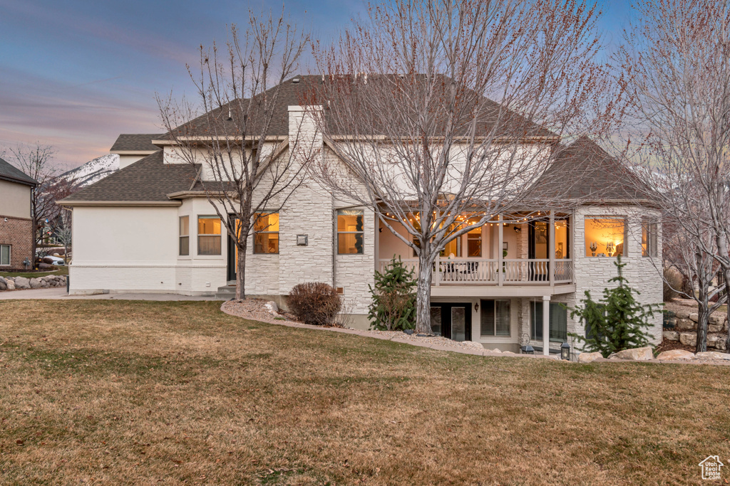 Back of property with stone siding, stucco siding, a shingled roof, and a lawn