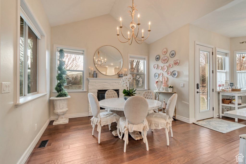 Dining room featuring a notable chandelier, hardwood / wood-style flooring, vaulted ceiling, and visible vents