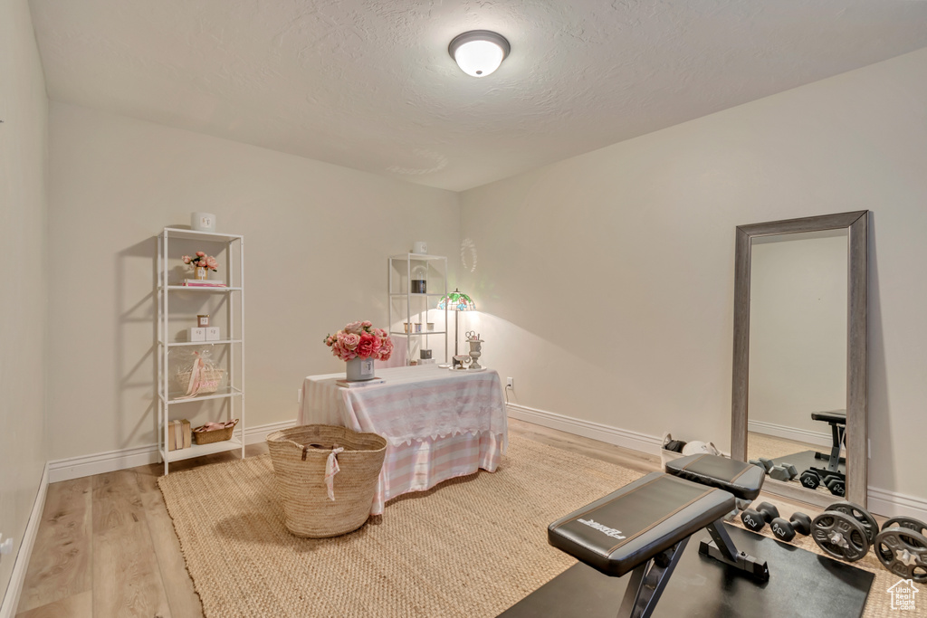 Exercise area featuring baseboards, a textured ceiling, and light wood-type flooring