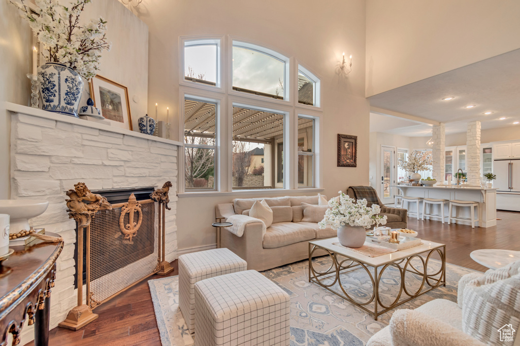Living room with a towering ceiling, a stone fireplace, and wood finished floors