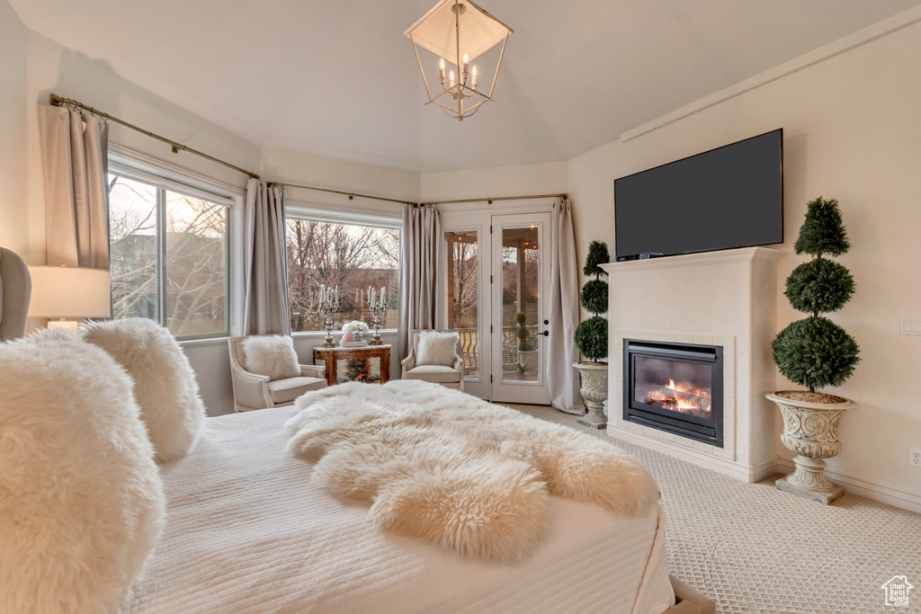 Carpeted bedroom featuring baseboards, access to exterior, a glass covered fireplace, and an inviting chandelier