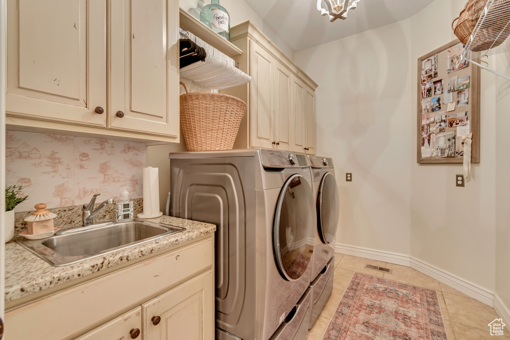 Laundry room featuring light tile patterned floors, baseboards, separate washer and dryer, a sink, and cabinet space